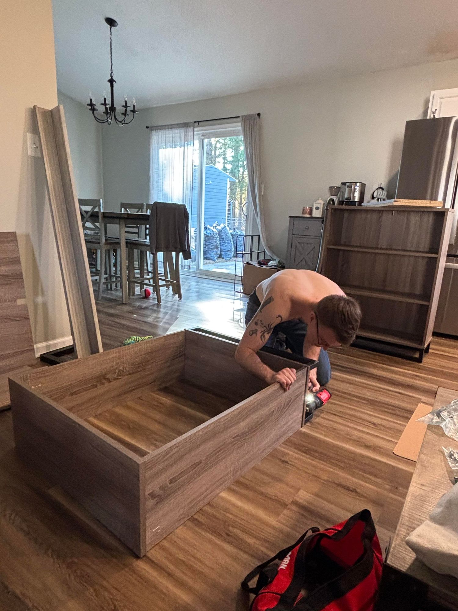 man assembling a large wooden bookshelf using a power drill in a modern living room.
