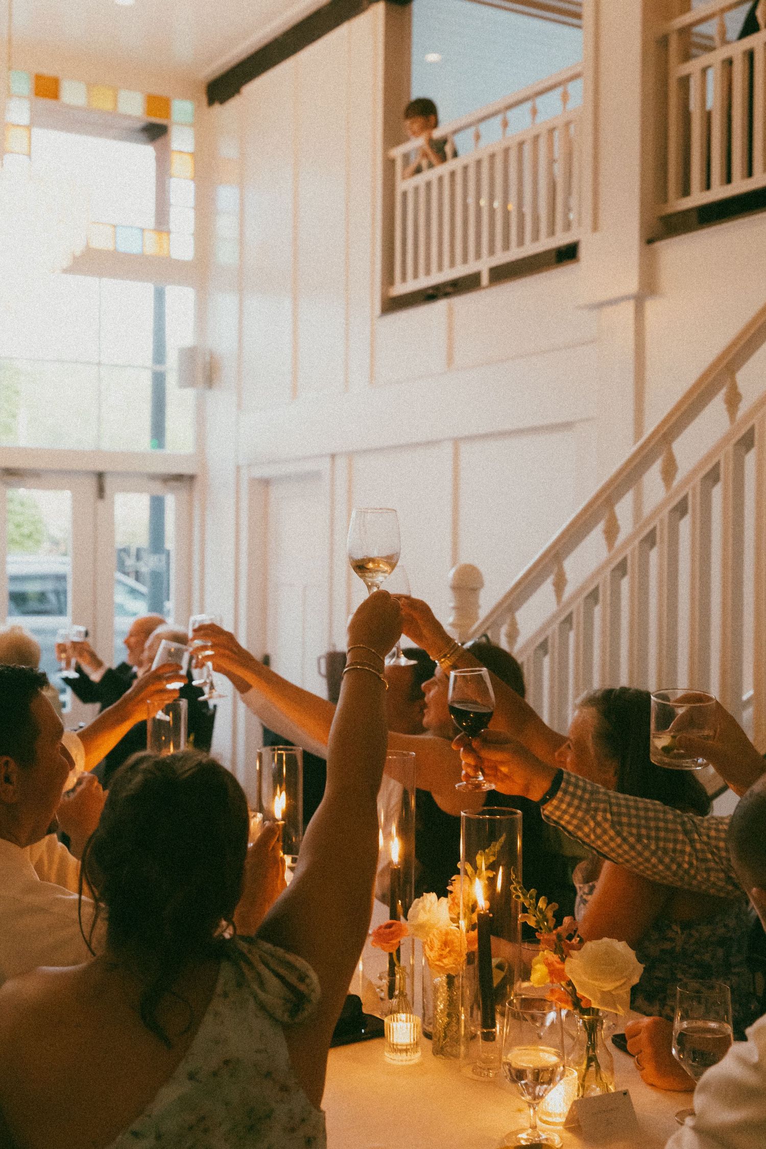 Guests raising wine glasses in a toast at an elegant indoor wedding reception at 128 south  with candlelit tables and white staircase.