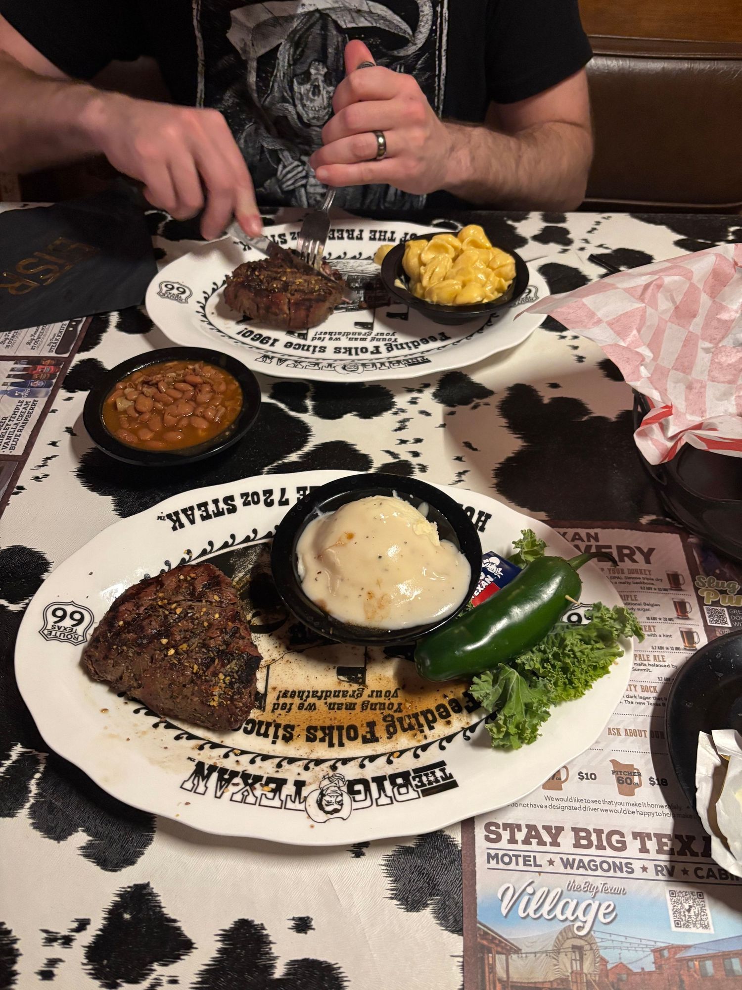 Two steaks with sides including mac and cheese, baked beans, and mashed potatoes served on Big Texan branded plates.