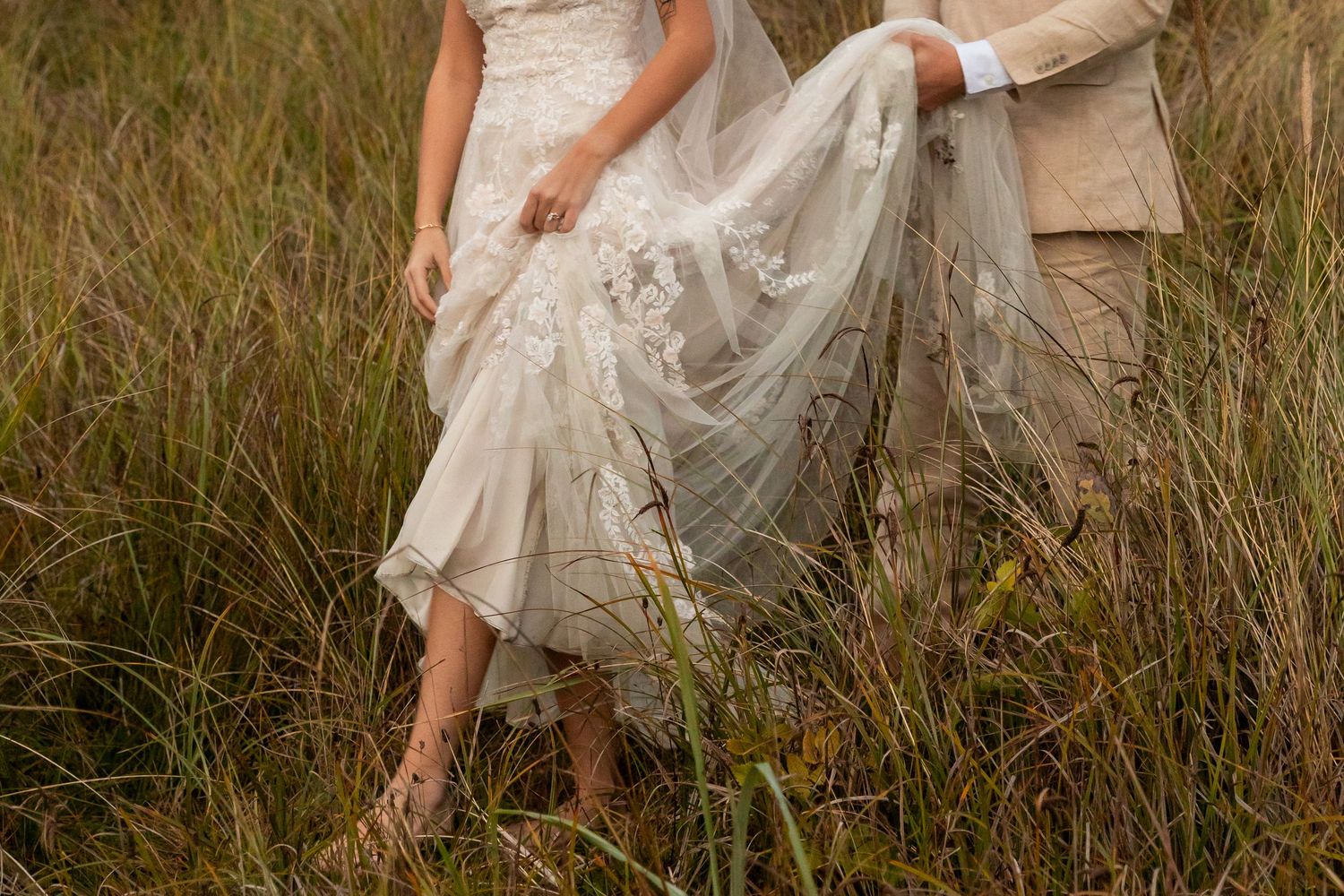 A bride in a flowing white dress walks through tall grass in a meadow at golden hour in North Carolina