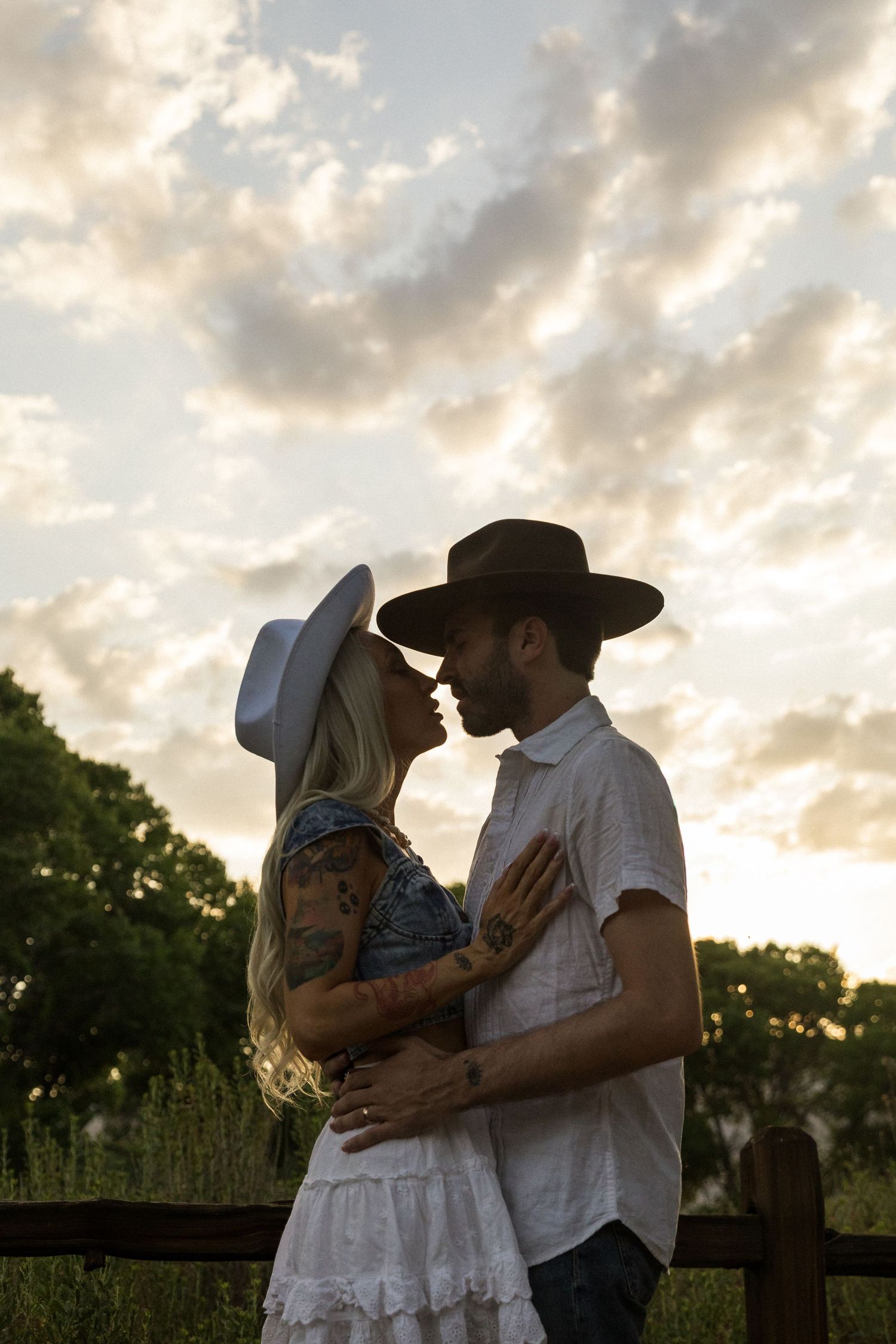 A romantic couple in western attire embraces during sunset against a dreamy sky backdrop in Jacksonville North Carolina