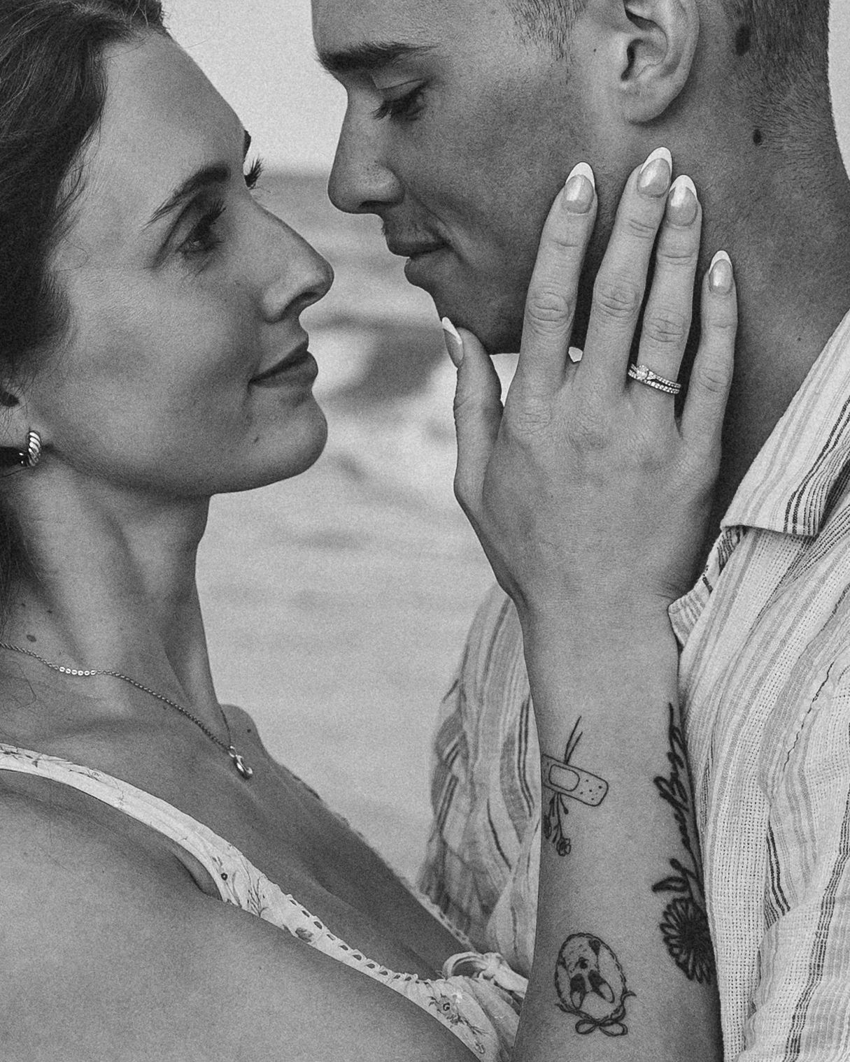 Black and white photo of a couple sharing an intimate moment, woman touching mans face, engagement ring visible on her hand.