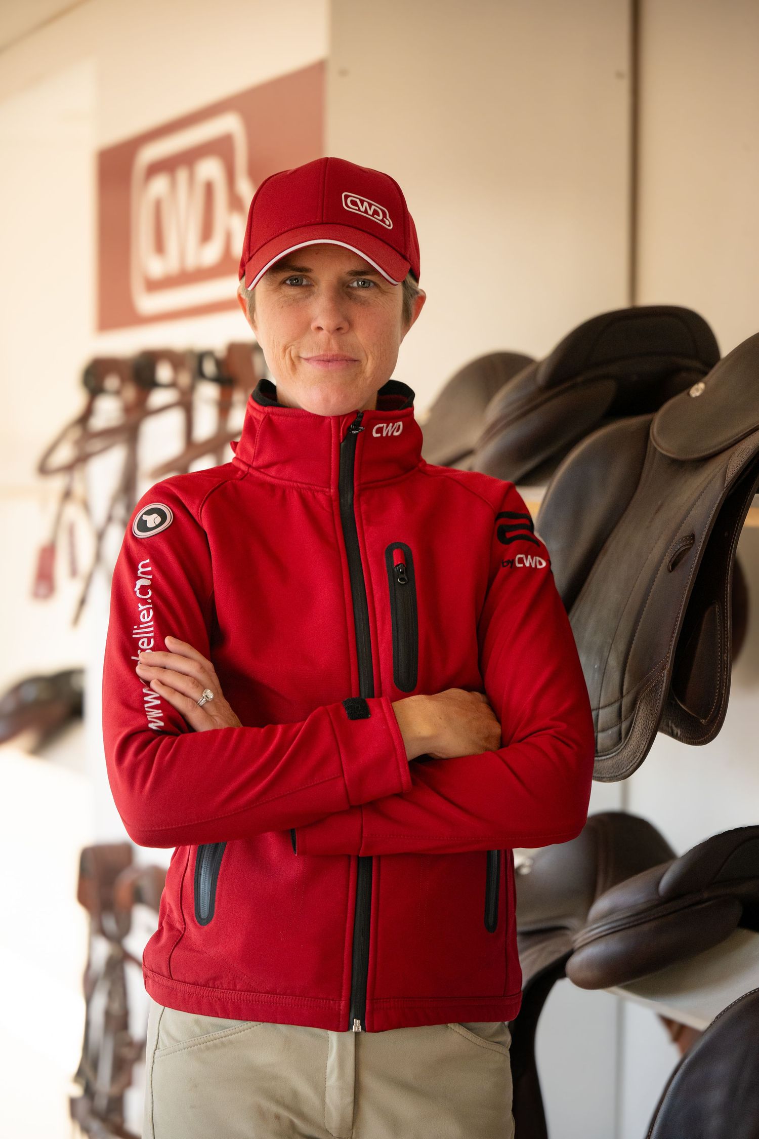 Woman in red CWD jacket and cap standing confidently in front of saddle display.