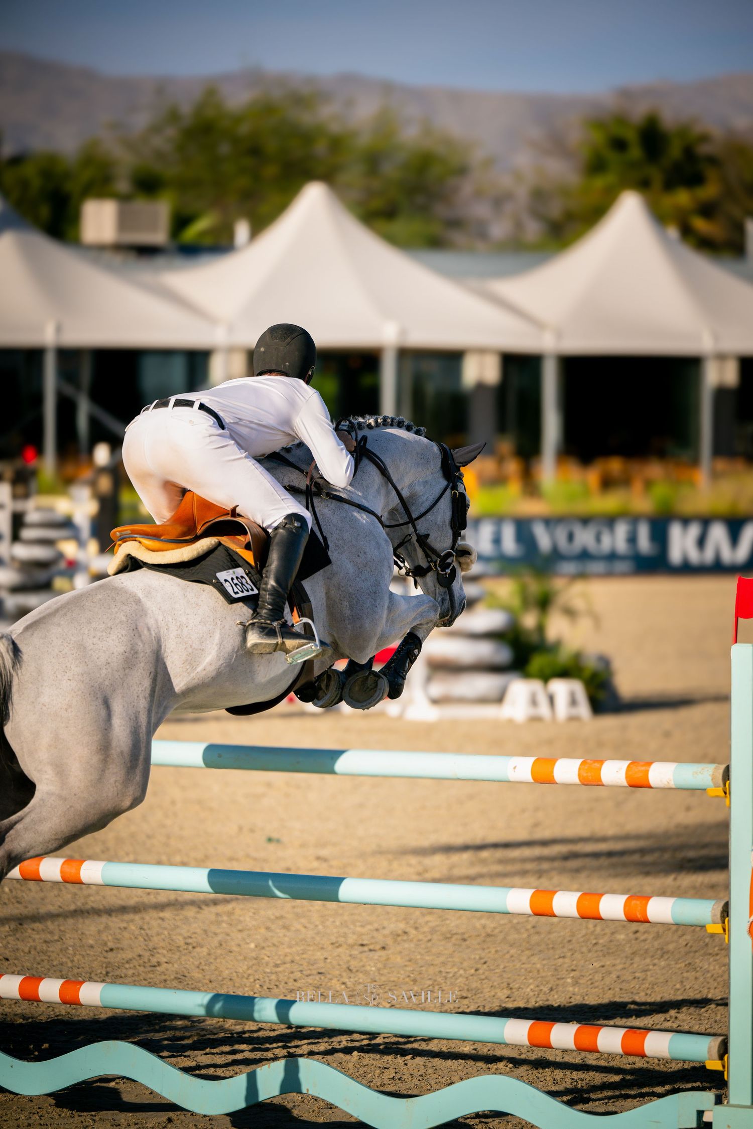 Gray horse and rider jumping orange-striped fence at outdoor equestrian competition.