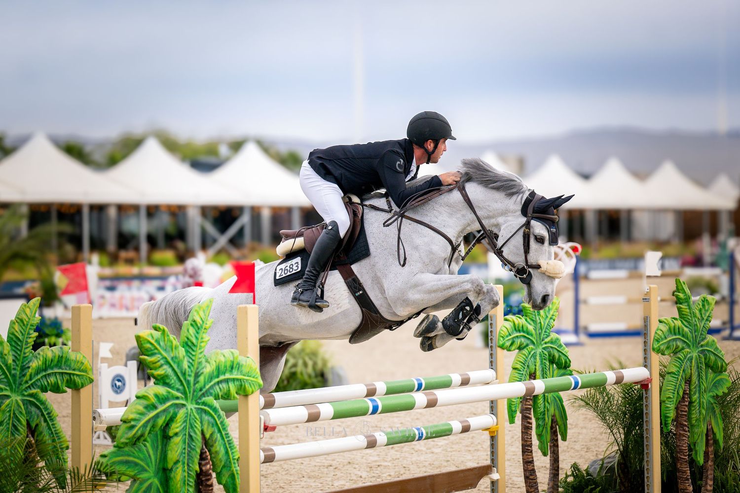 A rider on a white horse jumps over colorful hurdles at an equestrian show jumping competition.