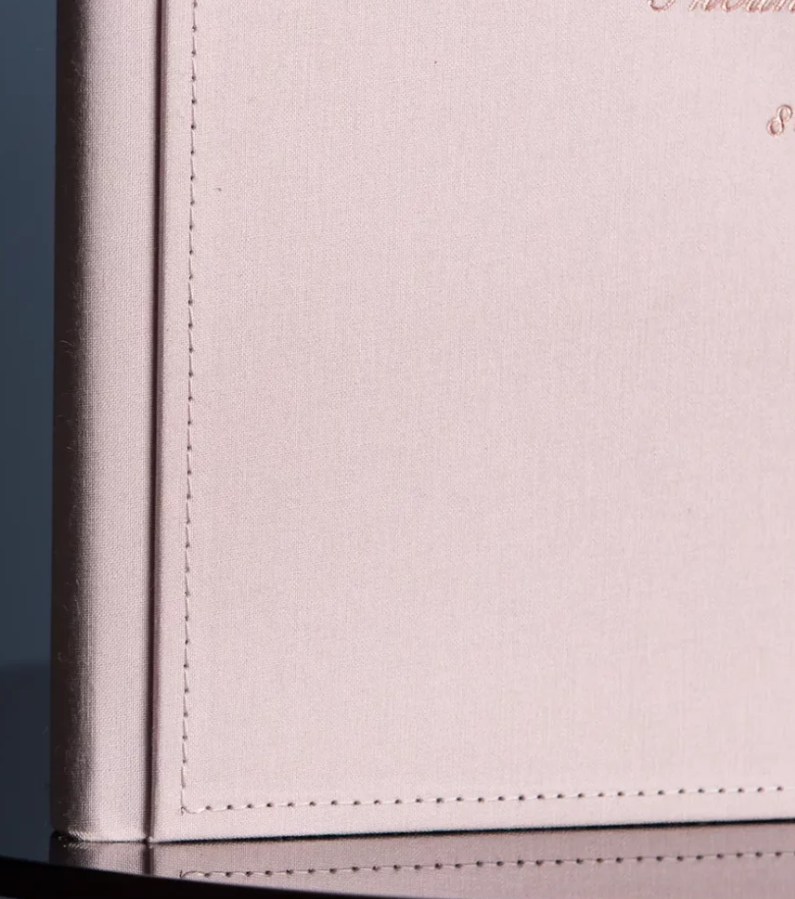 Close-up of a blush pink leather-bound journal with delicate stitched border detailing and rose gold embossed text.