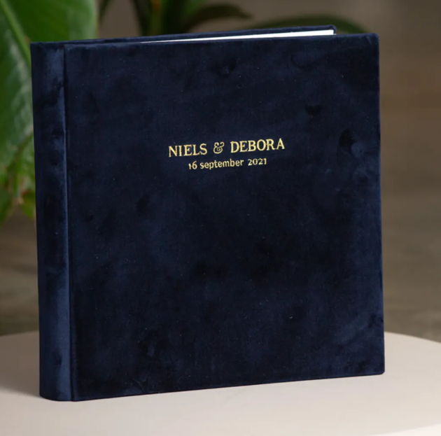 Navy blue velvet wedding photo album personalized with gold foil text reading Niels & Debora, 16 September 2021.