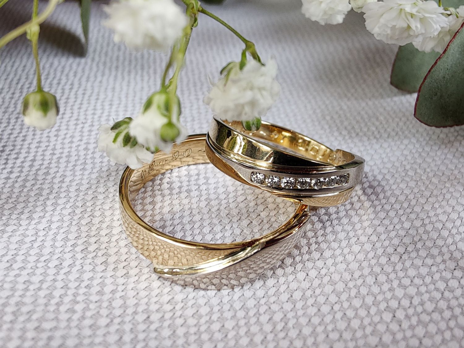 Twee gouden trouwringen, waarvan één met diamantjes, aan de bovenkant omzoomd door witte bloemen