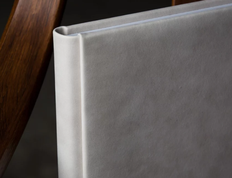 Close-up of a white leather-bound album resting against a wooden frame, showcasing premium craftsmanship and elegant design.