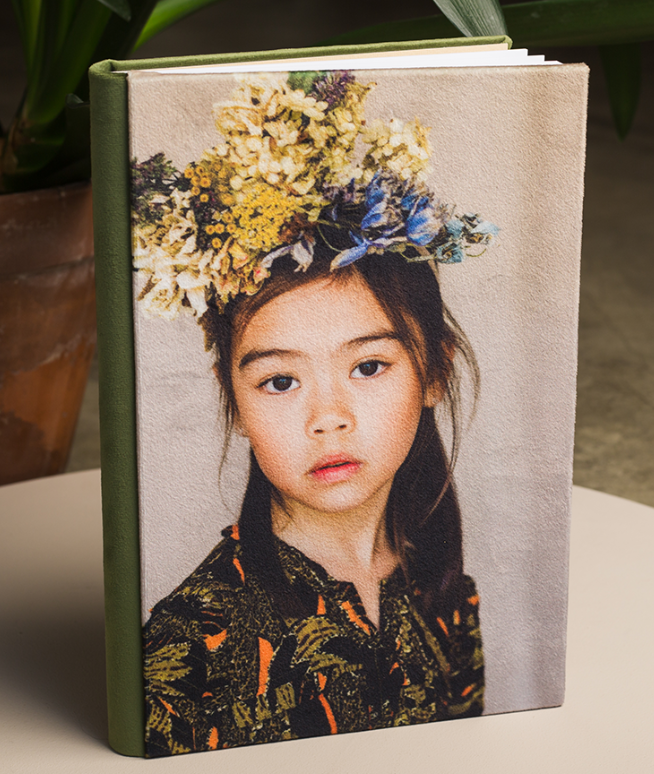 Hardcover photo book with a green spine and a cover portrait of a young child wearing a dried flower crown and a patterned dark top.
