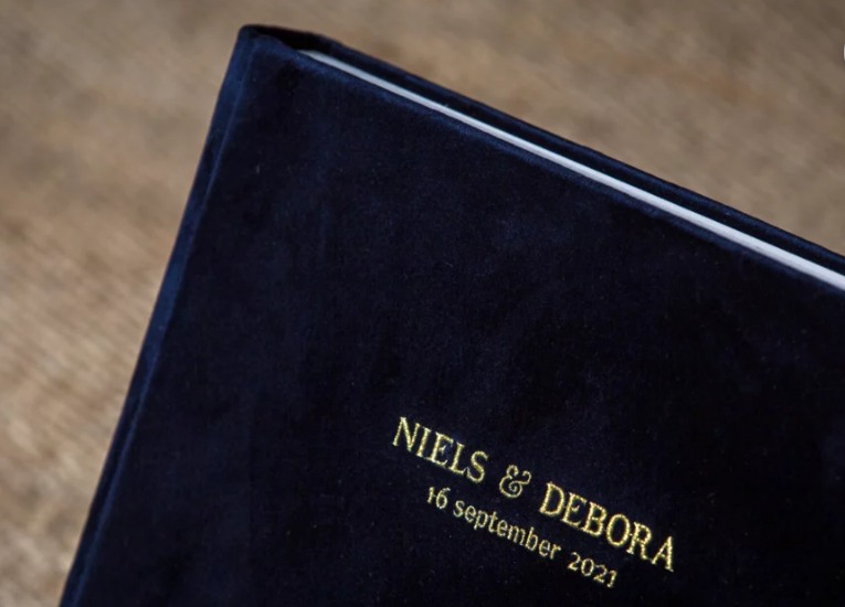 Navy blue velvet wedding album embossed with gold text reading Niels & Debora, 16 September 2021.
