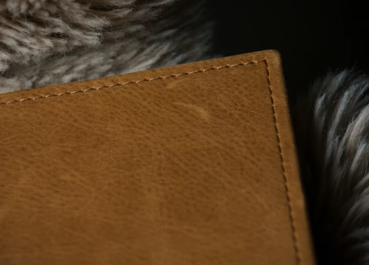Close-up of a tan leather wallet corner showing fine stitching detail against a soft fur background.
