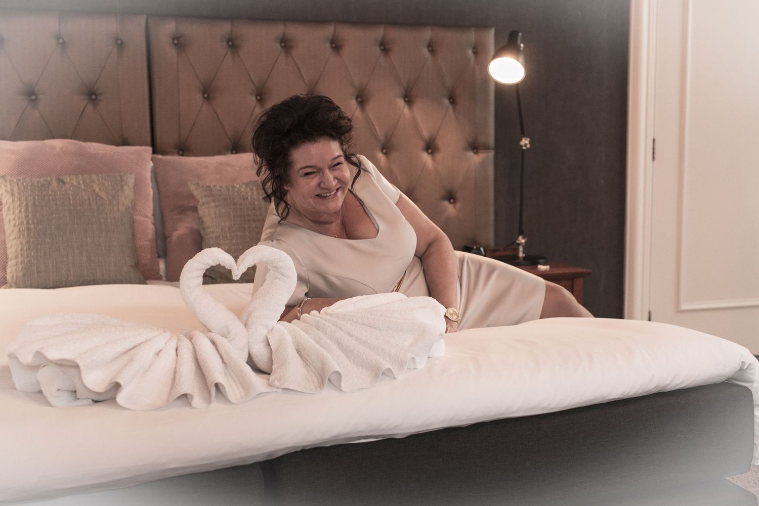 Woman relaxing on a luxury hotel bed with decorative swan towel folding arrangement in an elegant room.