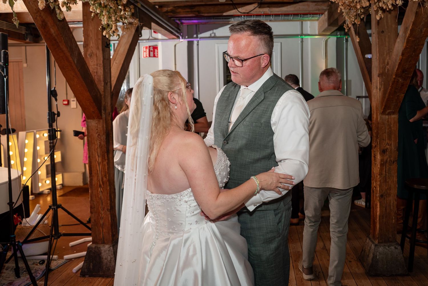 Bride and groom share their first dance at a rustic wedding venue with wooden beams and warm lighting.