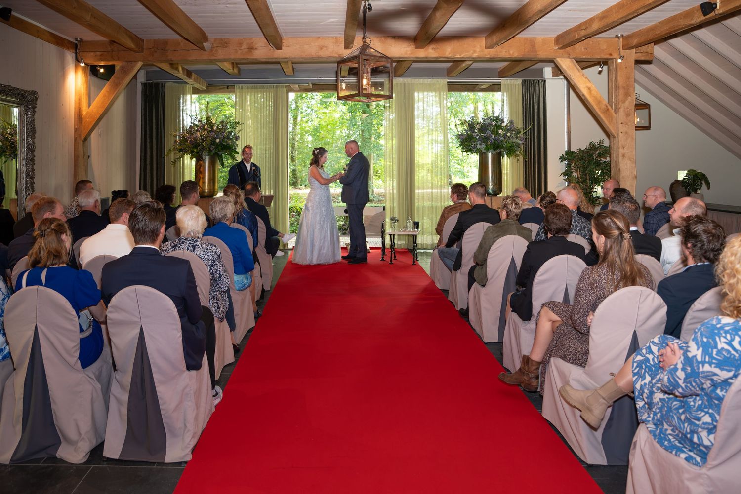 Bruidspaar staat voor grote ramen in de trouwzaal van De havixhorst. De bruid doet de trouwring om de vinger van de bruidegom. Met publiek.