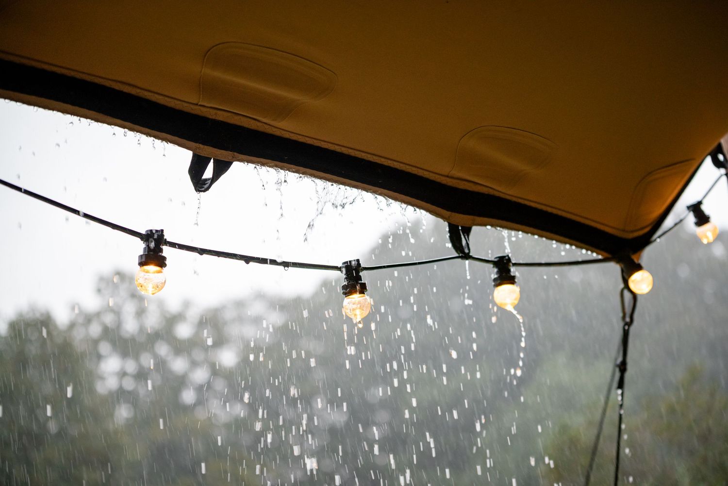 Een heftige regenbui valt op het doek van een stretchtent en over de lampenslingers die daar aan hangen.