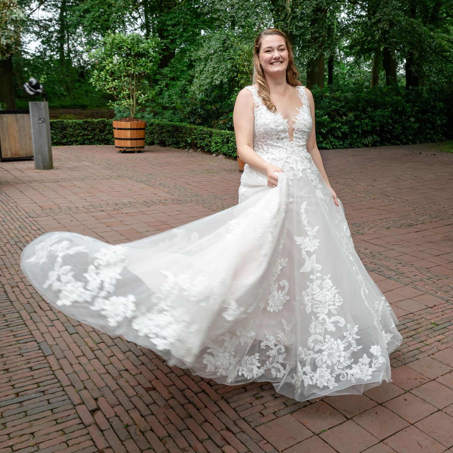Bruid swingt in haar witte trouwjurk waardoor haar jurk in de rondte gaat, op een terras van klinkers bij trouwlocatie De Havixhorst