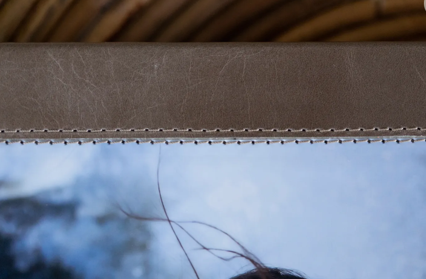 Close-up of a leather-bound frame with decorative stitching, partially revealing a blurred outdoor scene below.