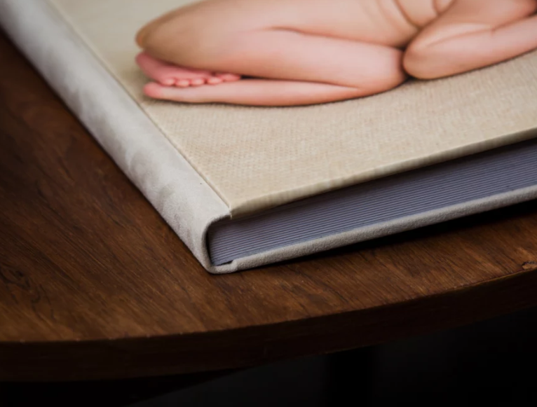 Close-up of a linen-covered photo album on a wooden table featuring a newborn baby photograph on the cover.
