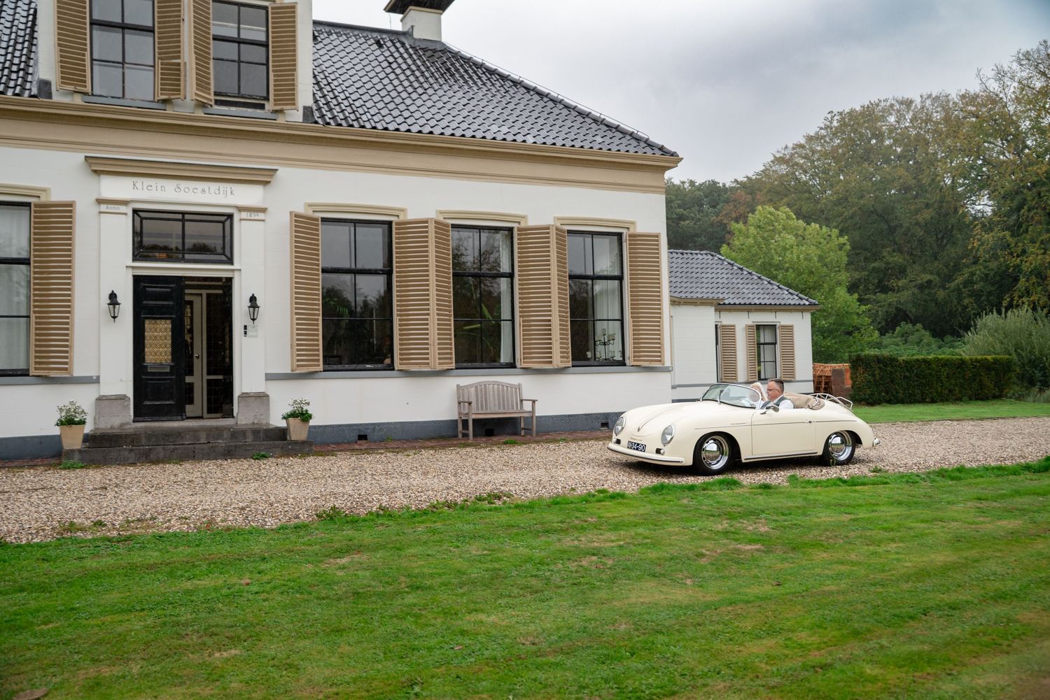 Bruidspaar arriveert in witte Vintage witte Porsche 356 cabrio op grindpad van trouwlocatie Klein Soestdijk in Veenhuizen,  Drenthe