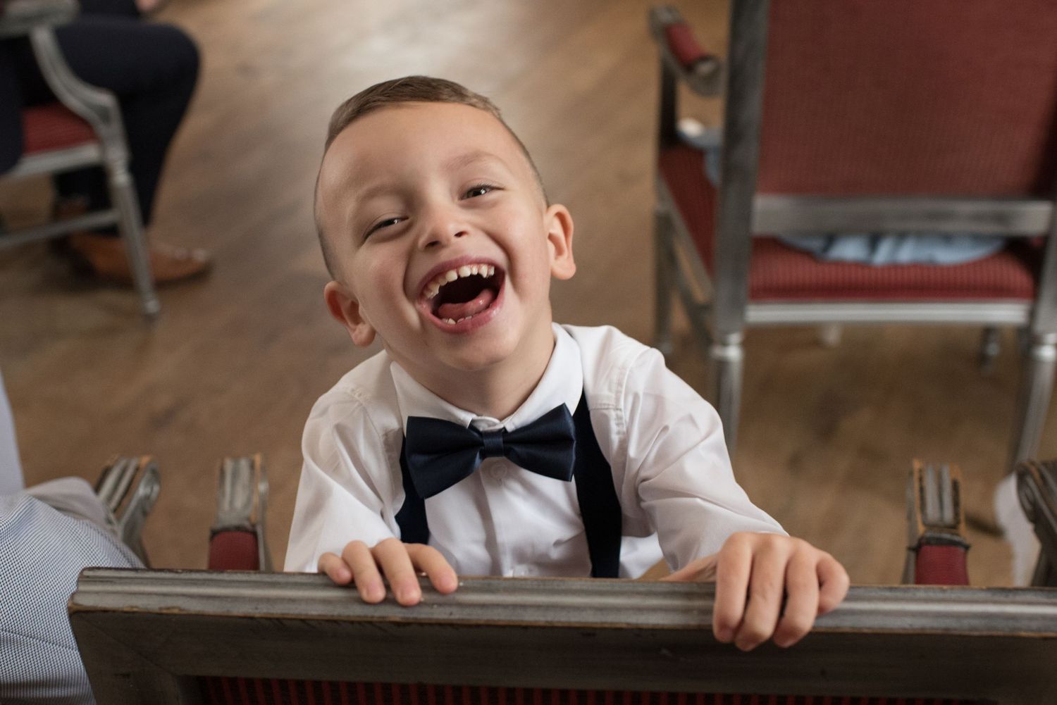 A joyful young boy in a white shirt and black bow tie laughs brightly at a formal event.