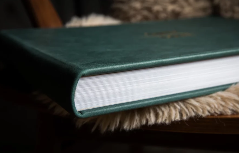 Close-up of a thick green leather hardcover book resting on a fluffy fur surface.