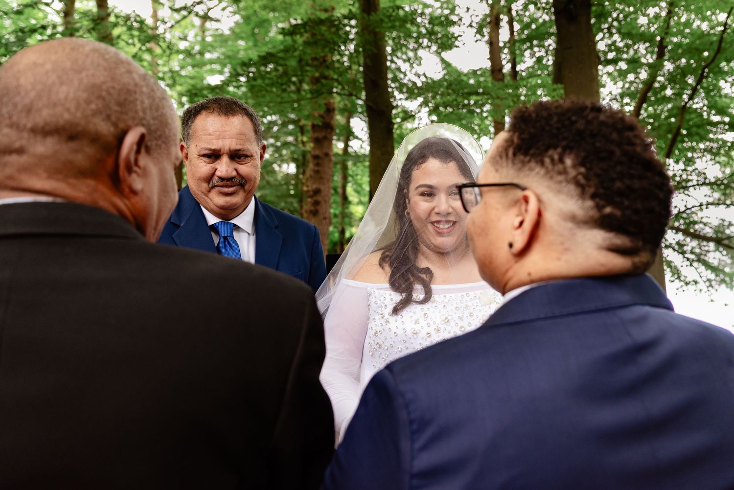 Bride smiling joyfully during an outdoor woodland wedding ceremony surrounded by guests and officiant.