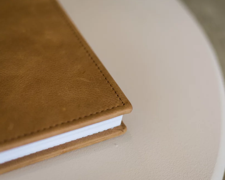Close-up of a tan leather hardcover journal with stitched binding resting on a white round table.