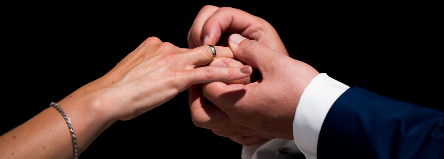 Close-up of a groom placing a gold wedding ring on the bride's finger during a marriage ceremony.