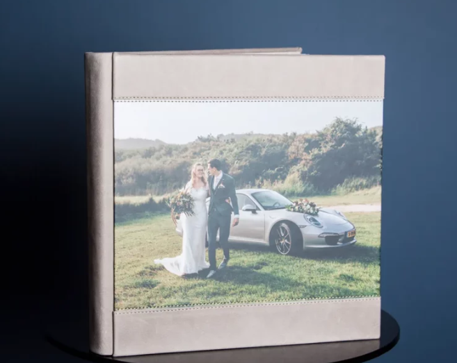 Elegant wedding photo album with linen cover featuring bride and groom posing by a silver Porsche in a scenic outdoor setting.