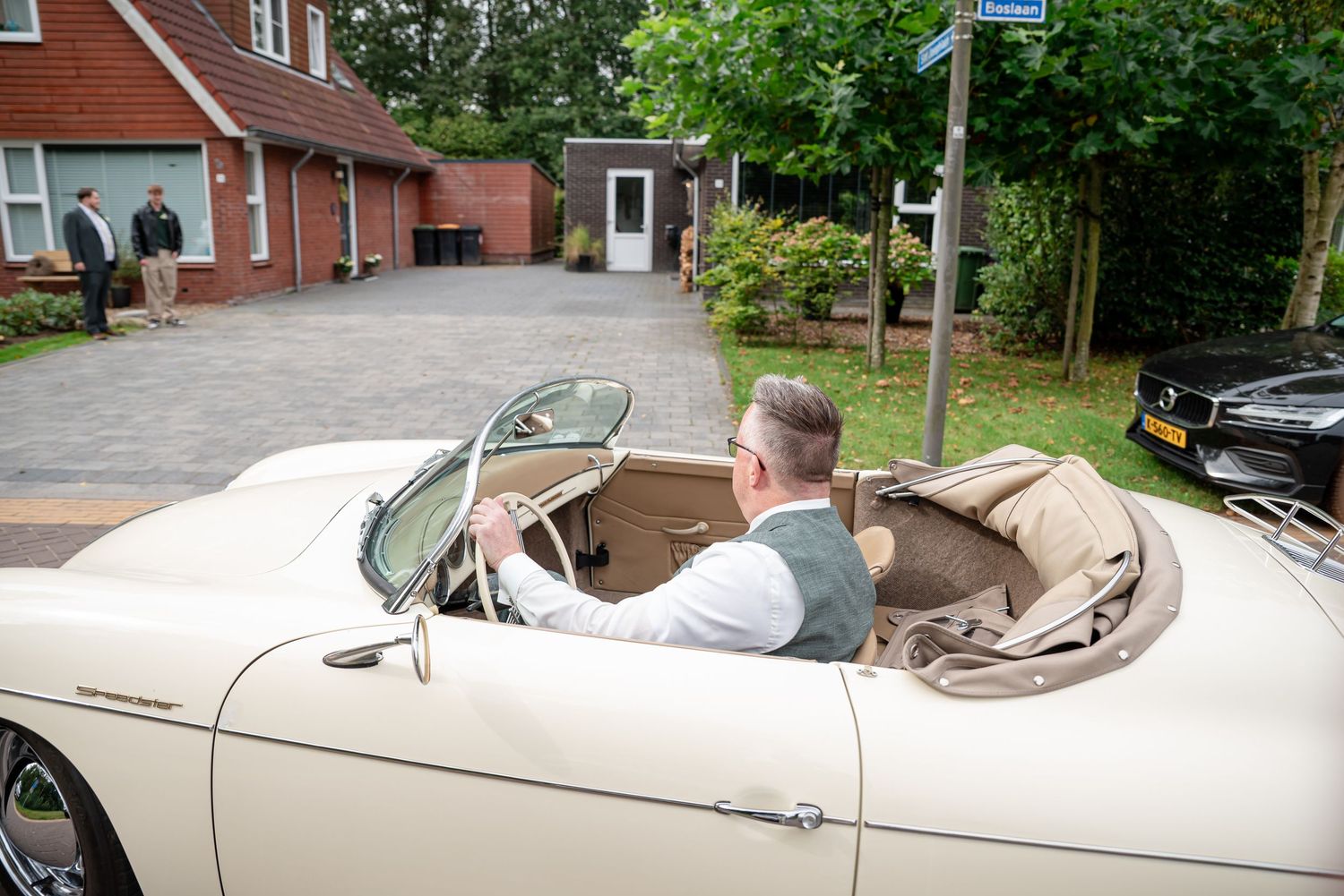 Bruidegom arriveert bij het huis van zijn bruid in een klassieke Porsche 356 cabrio. Achter het huis zie je groene loofbomen.