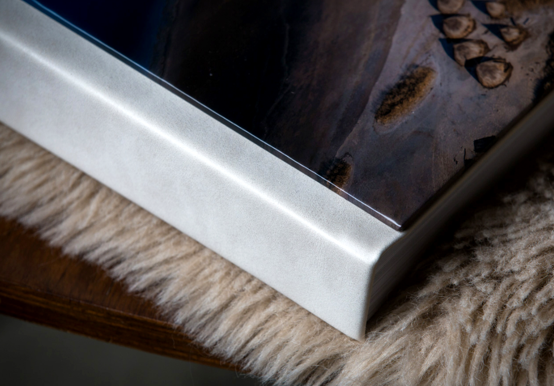 Close-up of a framed photo print with a white metal edge resting on a soft cream sheepskin rug beside a wooden surface.