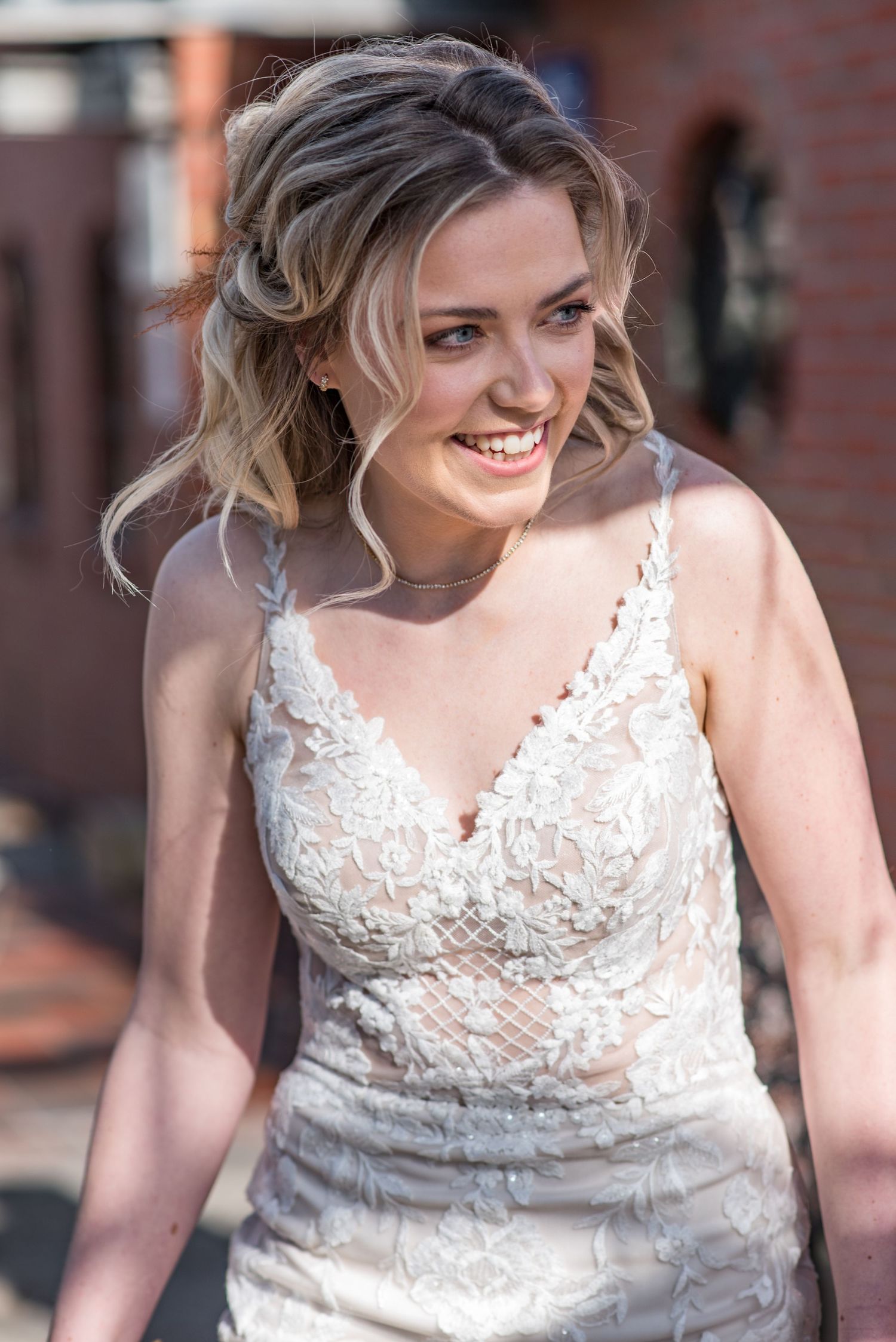Elegant opgemaakte bruid in witte trouwjurk met spaghettibandjes kijkt blij en enthousiast naar links