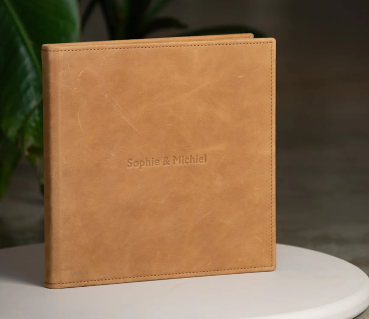 Tan leather photo album embossed with names Sophie & Michal, displayed on a white surface.
