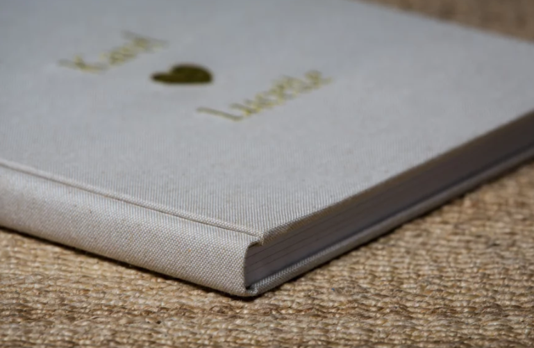 Elegant linen-covered wedding guest book with gold foil names and heart detail on textured fabric background.