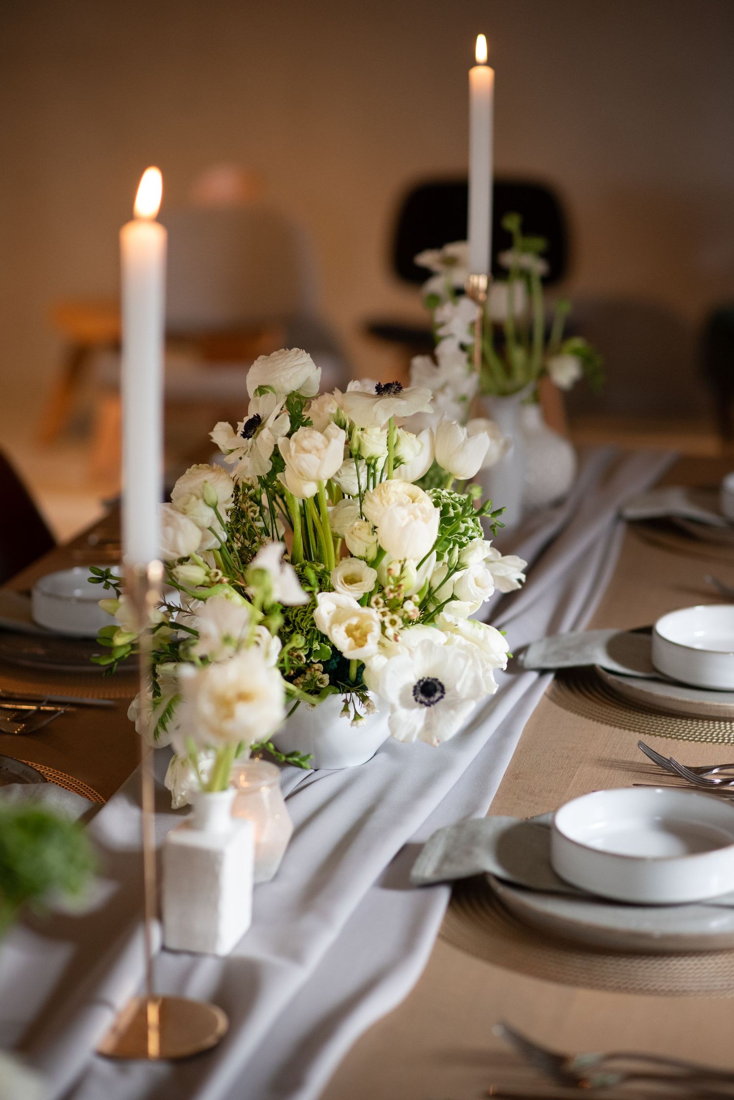 De tafel voor een bruiloft is smaakvol opgemaakt met een witte chiffon tafelloper, witte kaarsen en witte rozen, gipskruid en eucalyptus.