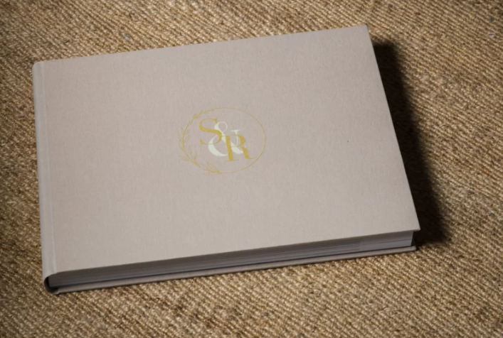 Elegant gray hardcover book with gold monogram embossed logo on textured linen surface.