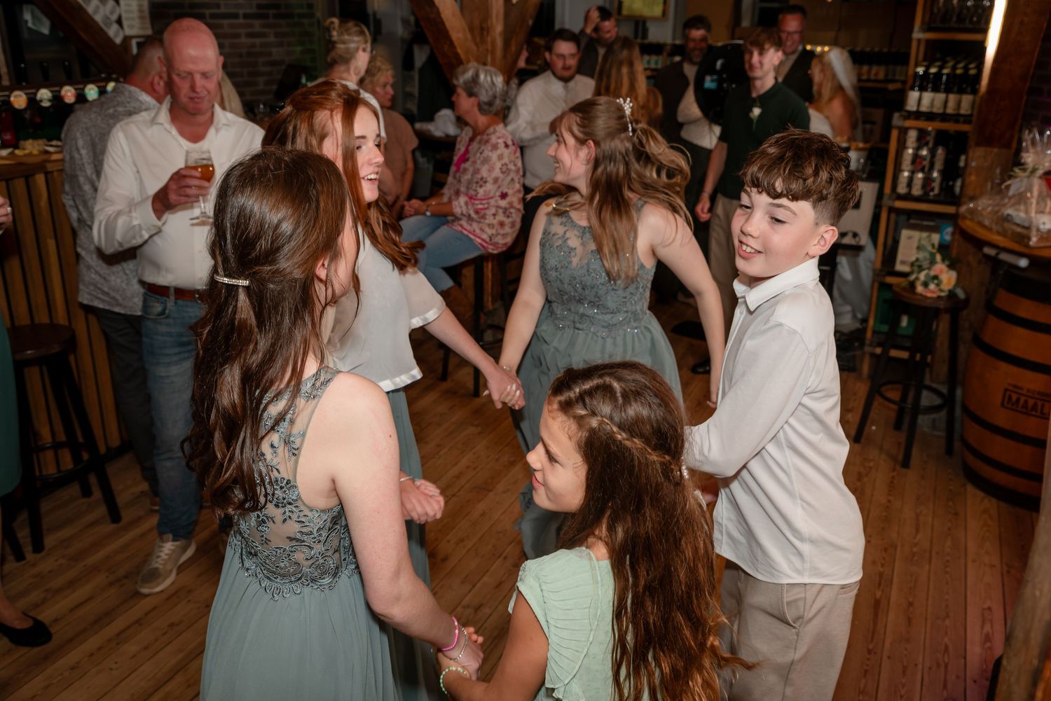 Children and teens in formal attire dancing together at an indoor wedding reception celebration.