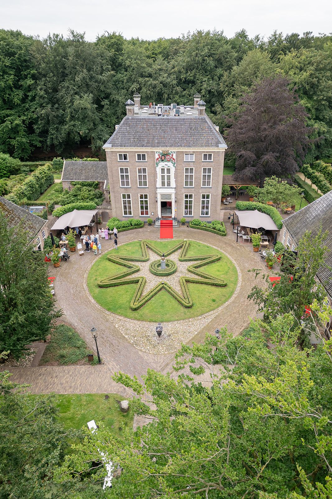 Dronefoto van het historische landhuis De Havixhorst, hier in gebruik als trouwlocatie. De rode loper ligt uit en links zijn bruiloftsgasten