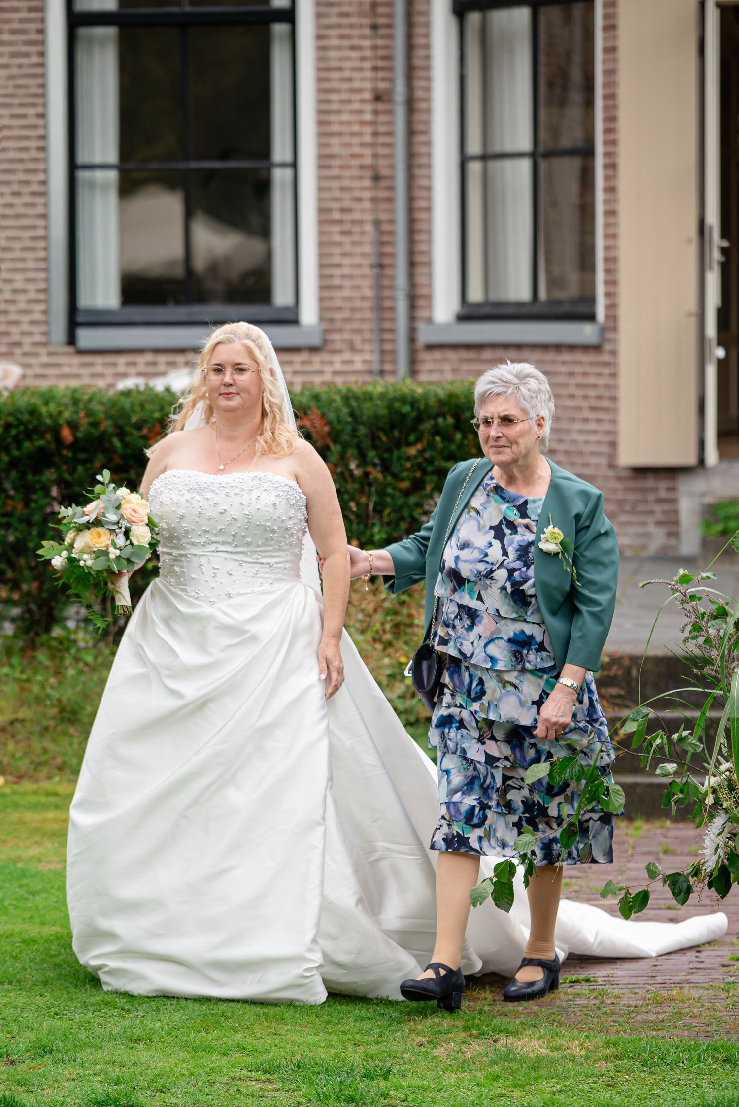 De Bruid loopt met haar moeder de tuin in van de trouwlocatie waar het altaar staat.
