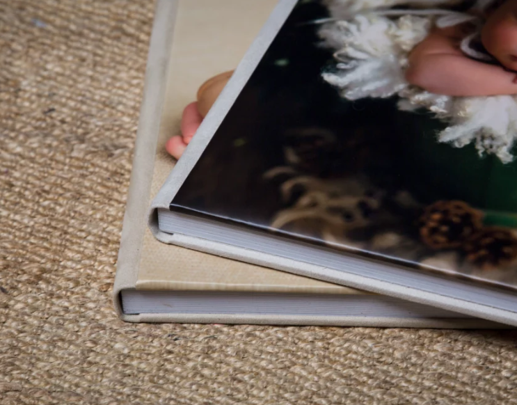 Two hardcover photo books stacked on a carpet, featuring a Christmas-themed cover with pine cones and holiday decor.