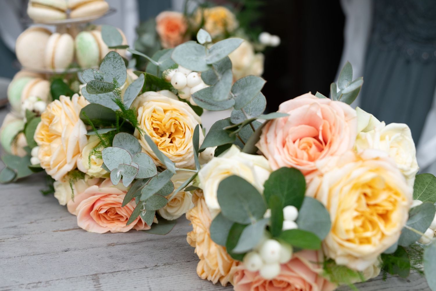 Two elegant wedding bouquets featuring peach and yellow roses with eucalyptus greenery displayed on a rustic surface.