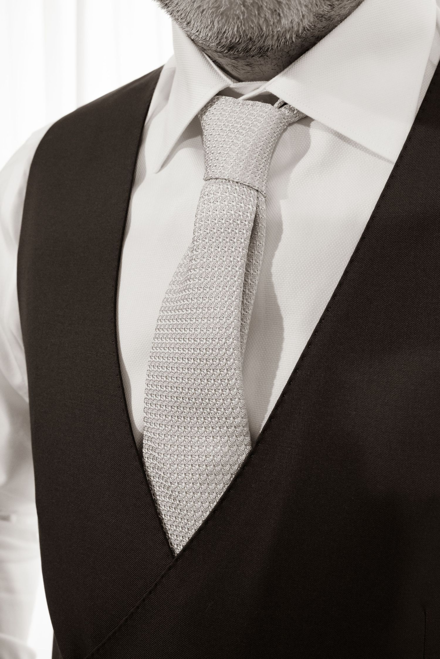 Close-up of a groom wearing a dark vest and silver knitted tie in a classic black and white photo.