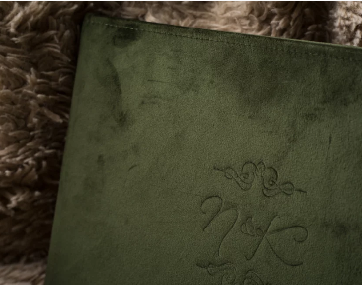 Green velvet album embossed with monogram initials N&K, resting on a textured fur surface.