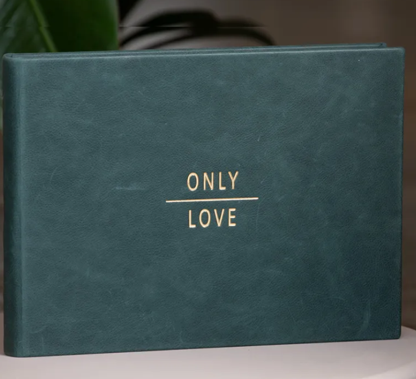 Teal green leather-bound guest book embossed with gold text reading Only Love, displayed against a soft background.