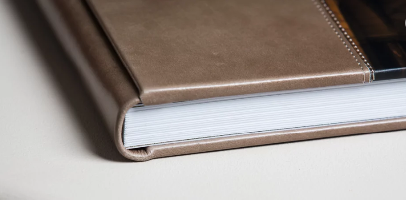 Close-up of a brown leather hardcover journal with white pages on a light surface.