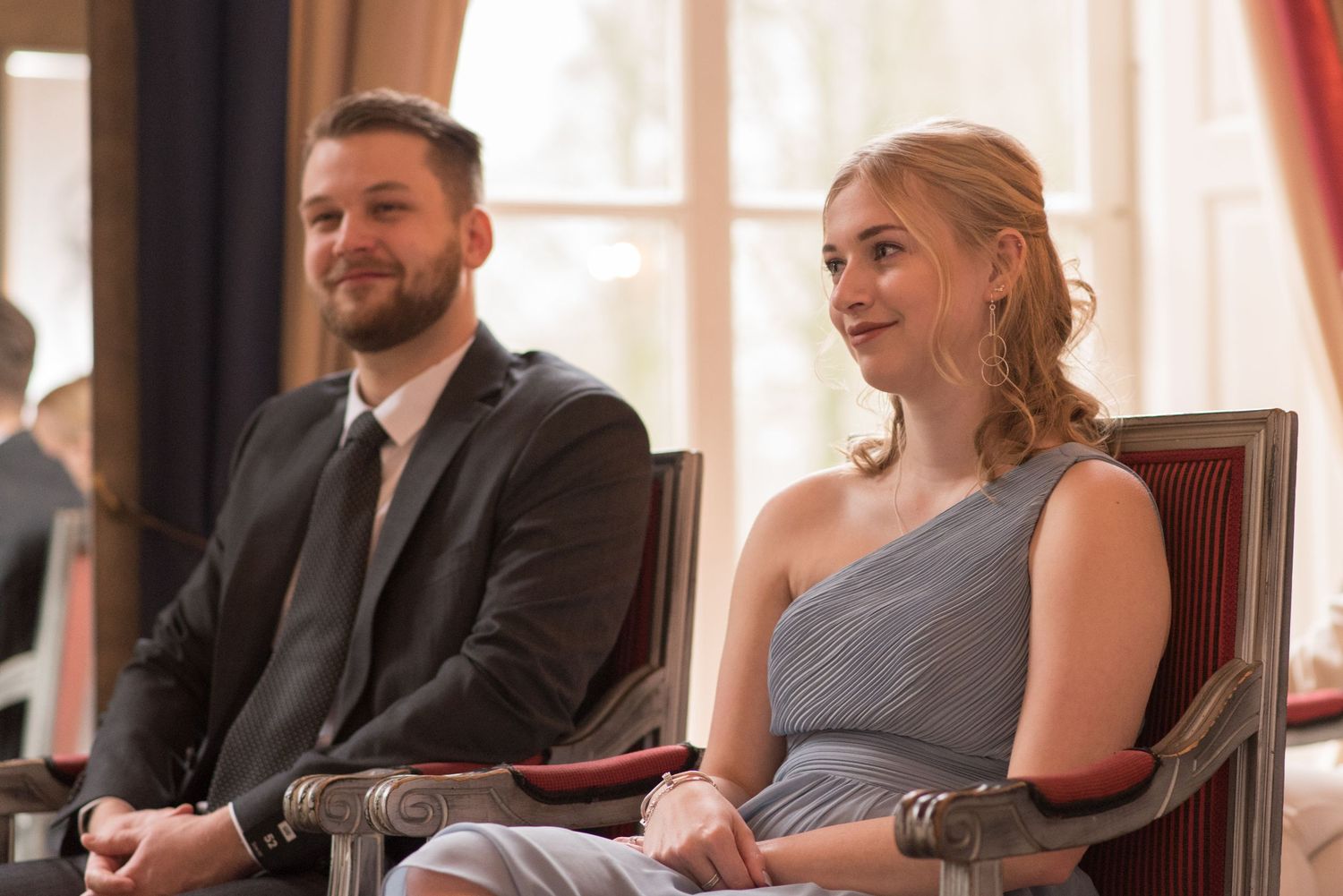 A smiling man and woman in formal attire seated together at an elegant indoor event.