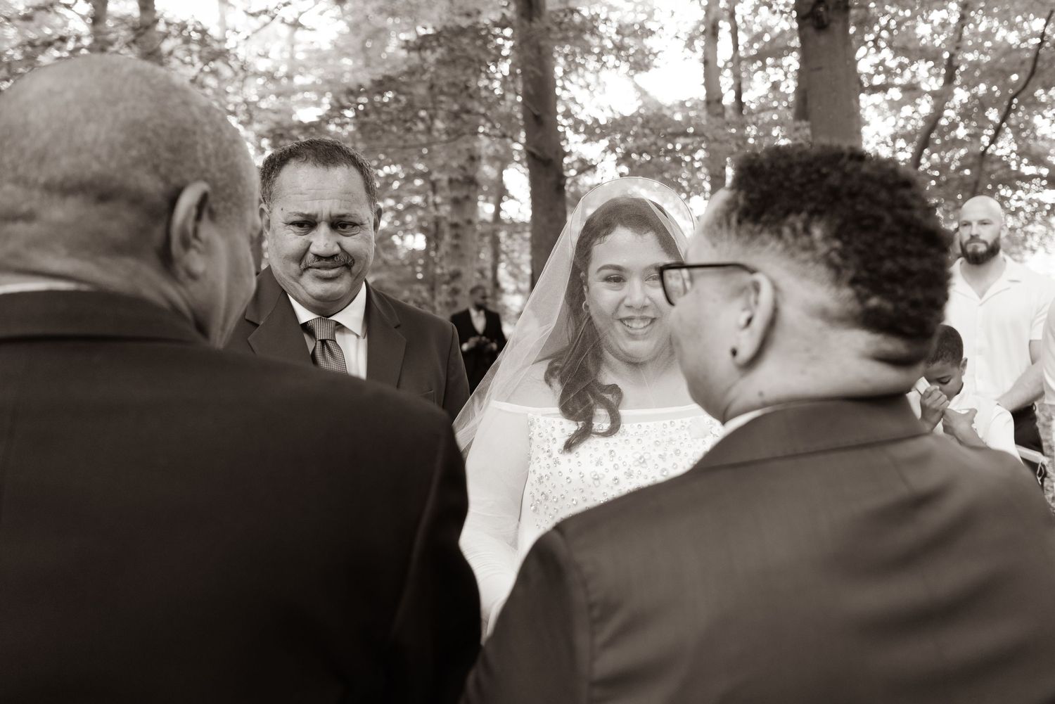 Black and white photo of smiling bride and groom during outdoor wedding ceremony.
