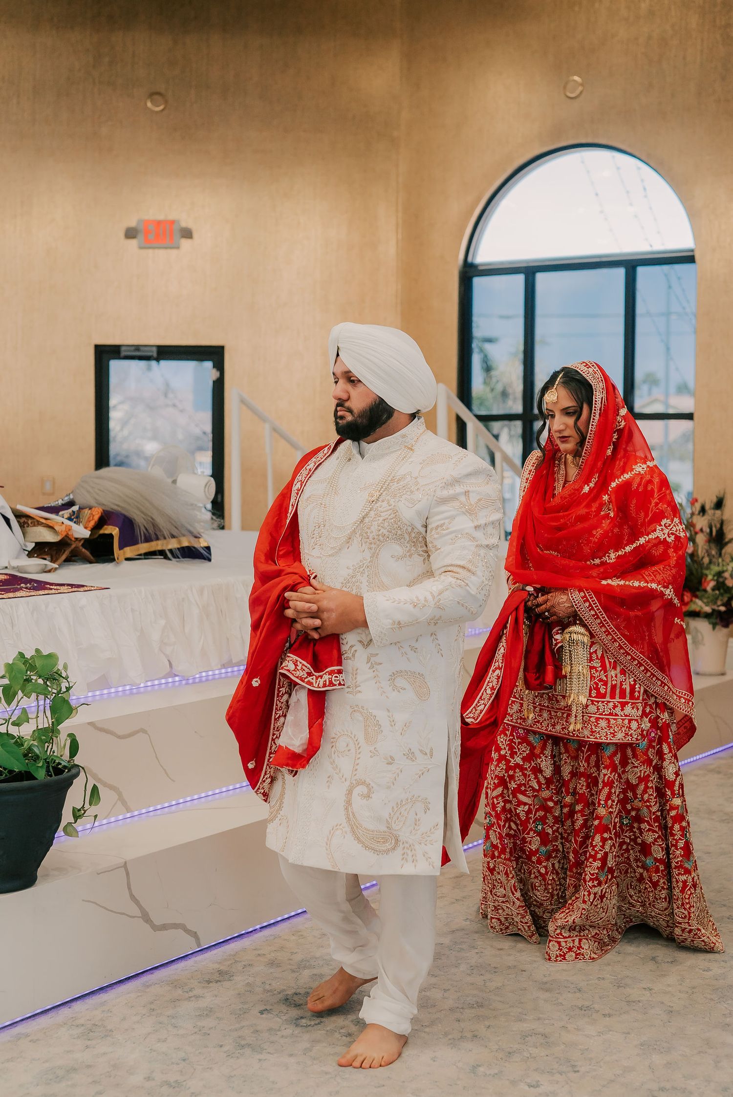 Sikh bride and groom in red and white traditional attire during Anand Karaj wedding ceremony.