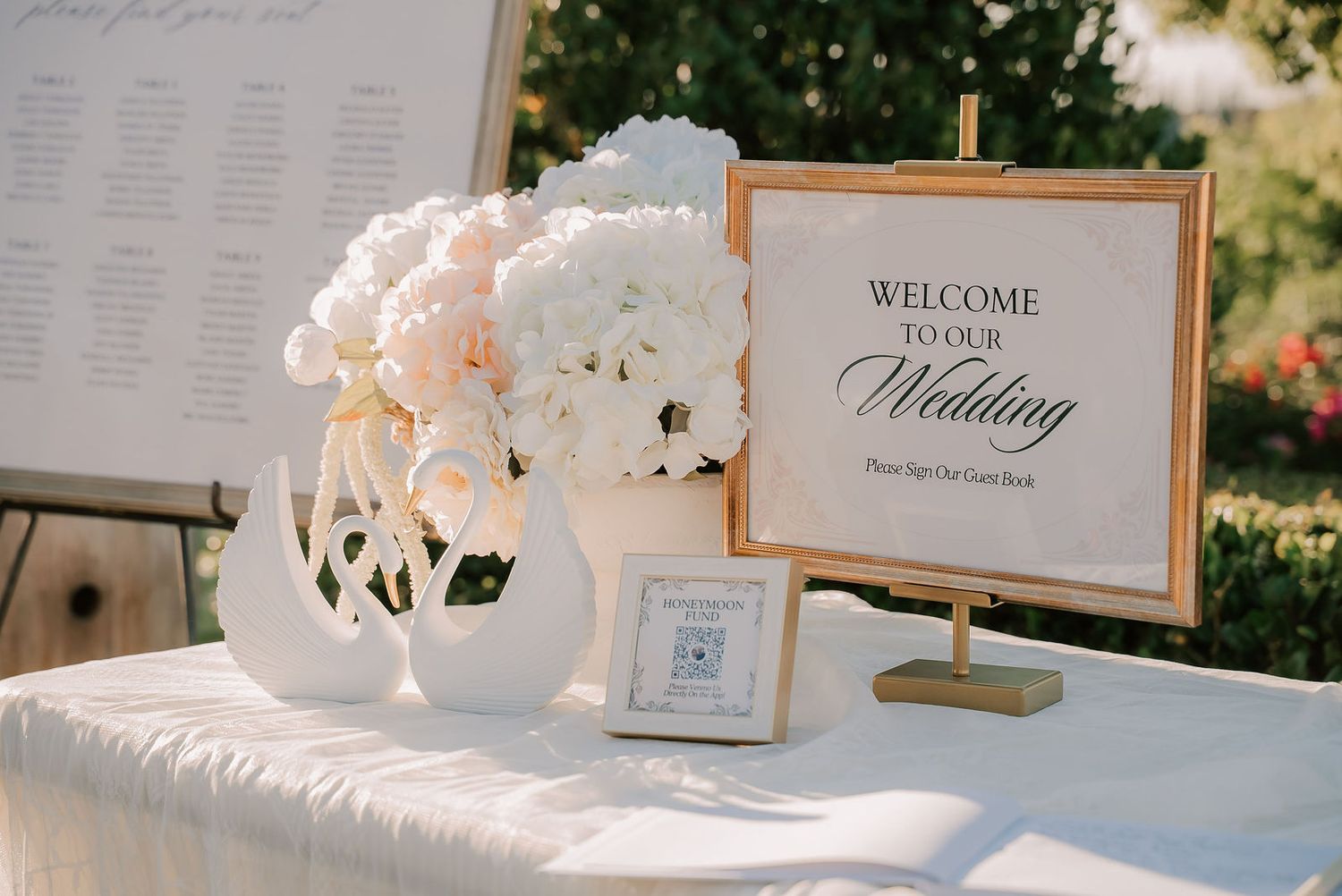 Elegant wedding welcome table with white floral arrangements, champagne flutes, and a gold-framed welcome sign.